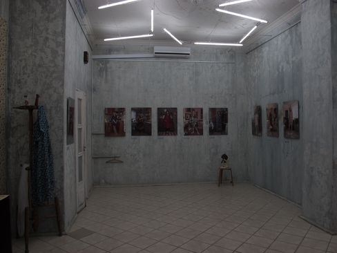 Dimly lit room with gray walls displaying several framed pictures and a ceiling with multiple fluorescent tubes arranged at angles.
