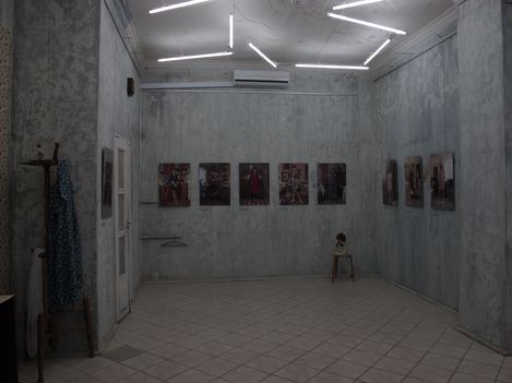 Dimly lit room with gray walls displaying several framed pictures and a ceiling with multiple fluorescent tubes arranged at angles.