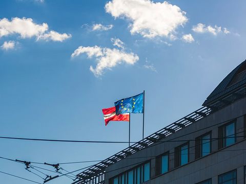 Auf einem Hausdach wehen zwei Fahnen, die Österreichfahne und die Europafahne.
