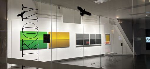Blick durch eine Glaswand mit der Aufschrift "EIKON" auf eine Galerie mit mehreren rechteckigen, farbigen Kunstwerken an der Wand und zwei schwarzen Vogel-Silhouetten auf der Glasfläche.