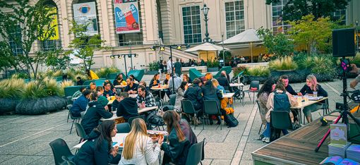 Several groups of people sitting at outdoor tables in front of a historic building with the inscription "FRANZ JOSEPH I. MDCCCLXIV".