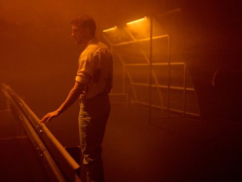 Man leaning on a railing in a foggy room lit with orange light