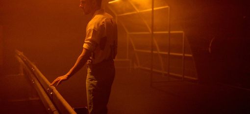 Man leaning on a railing in a foggy room lit with orange light