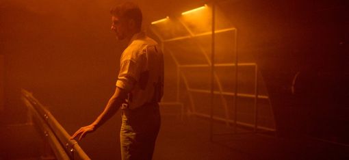 Man leaning on a railing in a foggy room lit with orange light