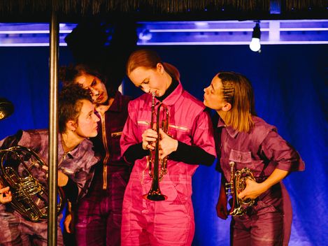 Auf dem Foto sind vier Frauen zu sehen. Alle haben Blechblasinstrumente in der Hand. Eine der Frauen spielt auf dem Instrument, die drei anderen beobachten sie neugierig und aufmerksam.