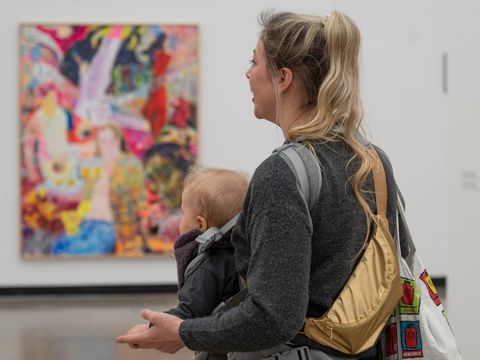 Eine Person mit Baby betrachtet ein Kunstwerk.