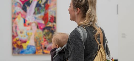 Eine Person mit Baby betrachtet ein Kunstwerk.