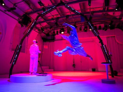 In a training laboratory for astronauts: the person dressed in white, seen from behind, is playing an instrument. The trainee takes a big leap and floats in the air.