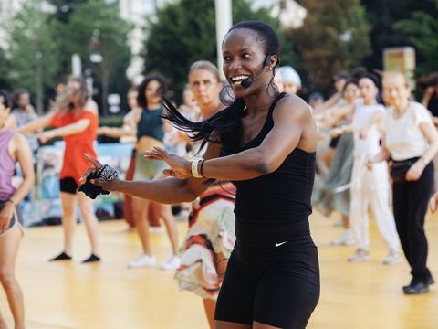 Frau mit Headset und Sportkleidung führt eine Gruppe von Menschen bei einem Outdoor-Fitnesskurs an