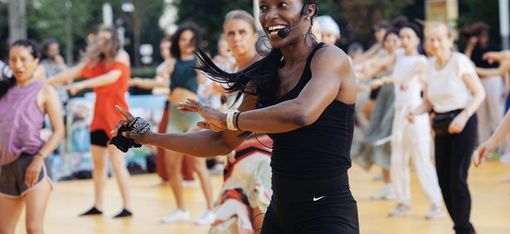 Frau mit Headset und Sportkleidung führt eine Gruppe von Menschen bei einem Outdoor-Fitnesskurs an