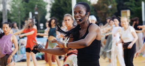 Frau mit Headset und Sportkleidung führt eine Gruppe von Menschen bei einem Outdoor-Fitnesskurs an