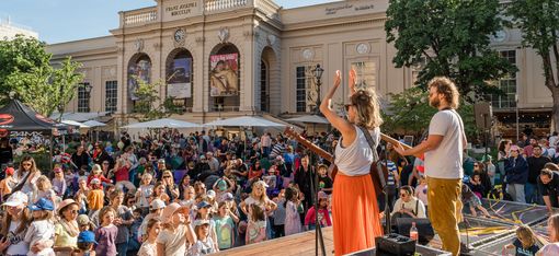 Open-Air-Konzert vor einem historischen Gebäude; begeistertes Publikum, Kinder tanzen, Musiker spielen.
