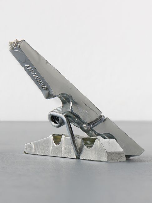 Close-up of a silver metal clamp with visible welds on a gray surface.