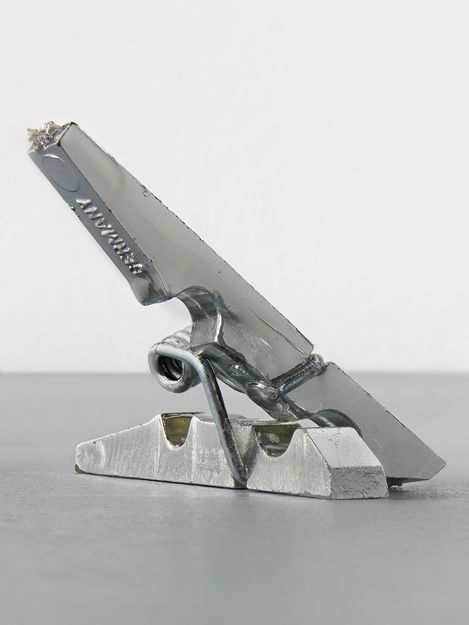 Close-up of a silver metal clamp with visible welds on a gray surface.