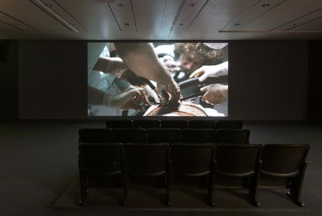 In einem dunklen Saal stehen Kinositze und auf einer Leinwand ist eine Szene aus dem Film Night Shift von Scott Clifford Evans zu sehen, in der eine Person operiert wird.