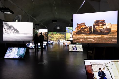 Two people stand in front of multiple large screens showing nature and portrait images
