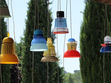Seven lamps, made from various plastic containers, are hanging in nature.