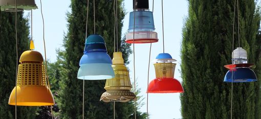 Sieben Lampen aus unterschiedlichen Plastikbehältern gefertigt, hängen in der Natur.