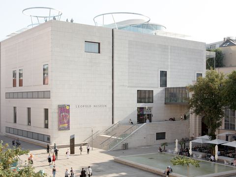 Kubischer Museumsbau des Leopold Museum mit hellen Steinfassaden und großen Fenstern vor einem Platz mit Menschen und Bäumen