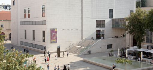 Kubischer Museumsbau des Leopold Museum mit hellen Steinfassaden und großen Fenstern vor einem Platz mit Menschen und Bäumen