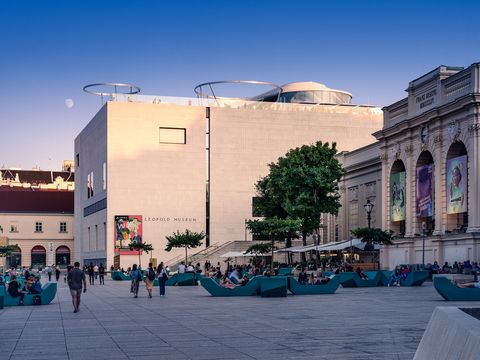 Leopold Museum with modern and historic architecture, a plaza with seating and people in daylight.