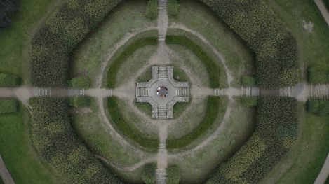Aerial view of a symmetrical circular garden with a central stone monument and four intersecting paths