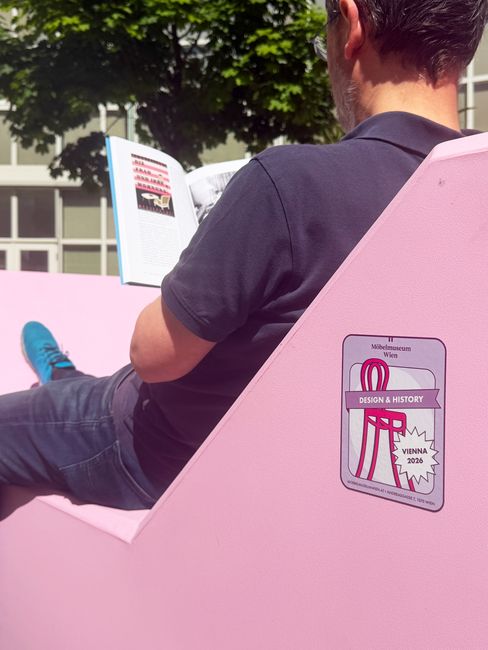 Person sitting on a pink Enzi reading a book; the “Enzi on Tour” graphic is visible on the side