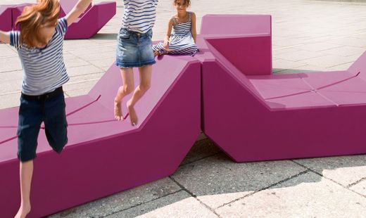 Three children in striped tops playing on modular pink seating in front of the Leopold Museum.