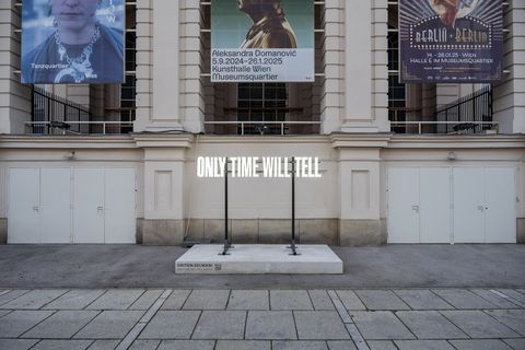 Illuminated text “Only Time Will Tell” by Driton Selmani in MuseumsQuartier Vienna in front of a historic facade.
