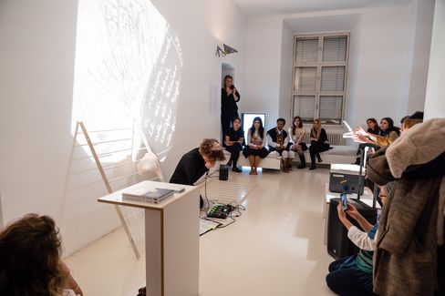 Person standing in front of a seated group in a bright room with a large window and projected graphic on the wall