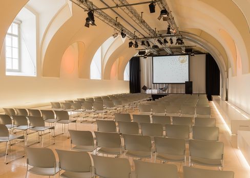 Leerer Veranstaltungsraum Arena21 im MuseumsQuartier Wien mit Reihen von Stühlen, gewölbter Decke und Leinwand am Bühnenende.