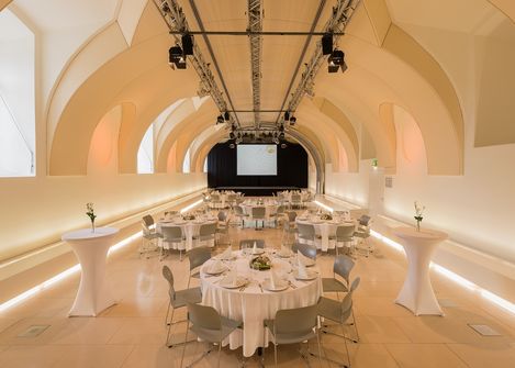 Großer Veranstaltungsraum Arena21 im MuseumsQuartier Wien mit gewölbter Decke, runden gedeckten Tischen und Stehtischen in hellem Ambiente.