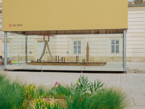 Außenansicht der MQ Art Box im MuseumsQuartier Wien mit Blick auf die Installation im Inneren und umgebende Grünflächen im Vordergrund.