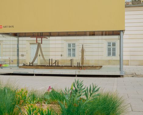 Außenansicht der MQ Art Box im MuseumsQuartier Wien mit Blick auf die Installation im Inneren und umgebende Grünflächen im Vordergrund.