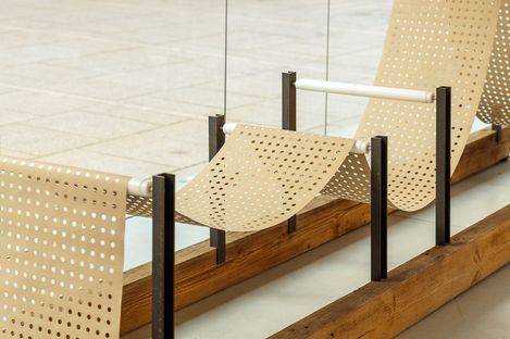 Detail of a perforated metal sheet stretched in a wave-like form between dark metal supports.