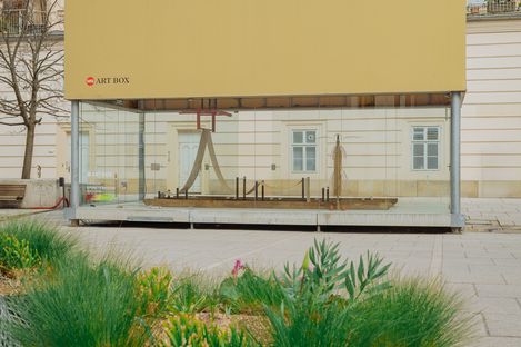 Exterior view of the MQ Art Box in MuseumsQuartier Vienna, showing the installation inside with greenery in the foreground.