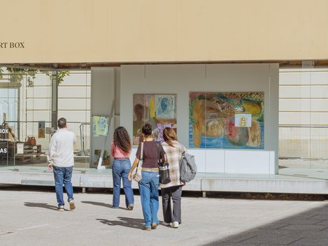 Four people walking toward a modern glass building with artworks displayed in the window