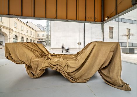 Close-up of the installation “ENZA” with sand-colored draped fabric forming a reclining shape in the space.