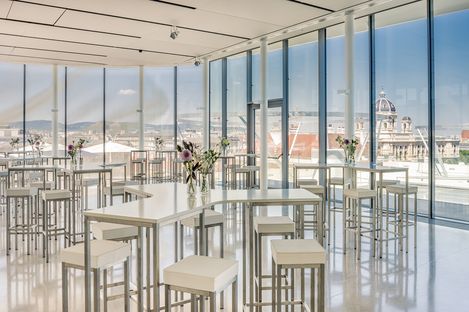 Moderner Veranstaltungsraum mit hohen Tischen und Hockern, großen Glasfenstern und Blick auf die Dächer von Wien und historische Gebäude.