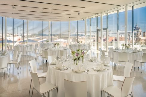 Heller, moderner Veranstaltungsraum mit runden, weiß gedeckten Tischen und weißen Stühlen, große Fenster mit Blick über Wien.