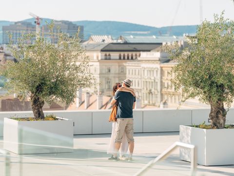 Paar umarmt sich auf der Dachterrasse der MQ Libelle mit großen weißen Pflanzkübeln und Stadtblick im Hintergrund.