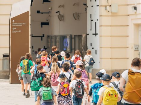 Eine Gruppe an jungen Kindern geht geführt von ihren Aufsichtspersonen durch die Innenhöfe des MQ.
