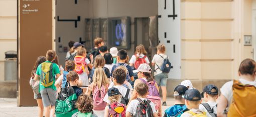 A group of young children, led by their supervisors, walks through the courtyards of the MQ.
