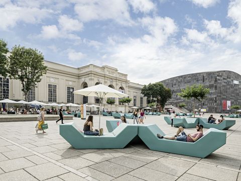 Menschen entspannen auf türkisfarbenen Enzi-Sitzmöbeln im Haupthof des MuseumsQuartier Wien, umgeben von historischer Architektur und dem mumok.