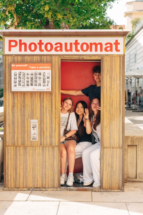 Group of young people sitting together inside a photo booth, smiling at the camera.