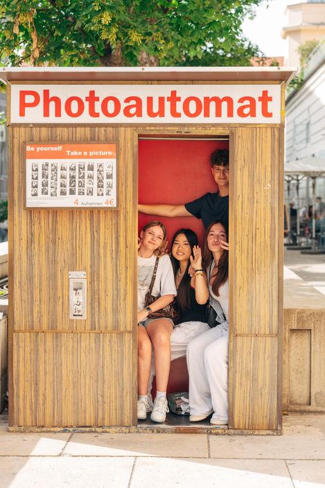 Group of young people sitting together inside a photo booth, smiling at the camera.