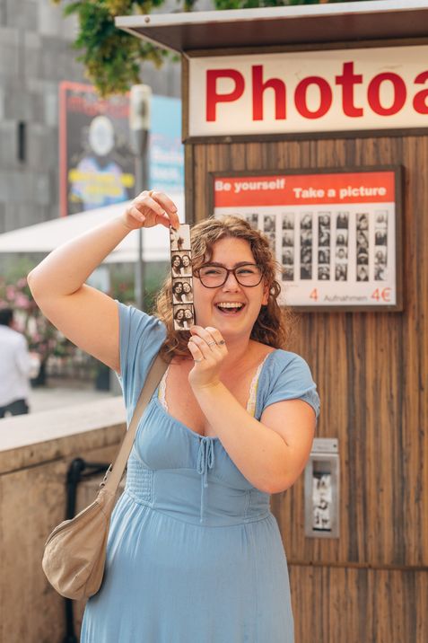 Woman holding a freshly developed photo strip in front of a photo booth, smiling.