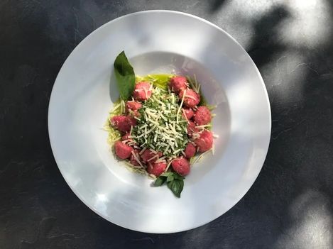 White plate photographed from above, with pink gnocchi topped with green pesto, cheese, and sage leaves arranged in the center.