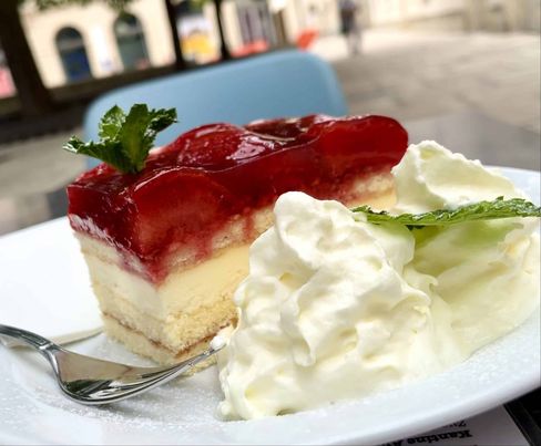 Fresh strawberry slices on a white plate. Served with mint, whipped cream, and a fork. A square in the background.