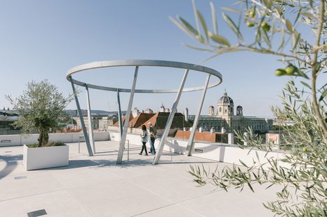 Öffentliche Terrasse MQ Libelle mit moderner, runder Metallstruktur und zwei Personen, Blick über Dächer und historische Gebäude Wiens.